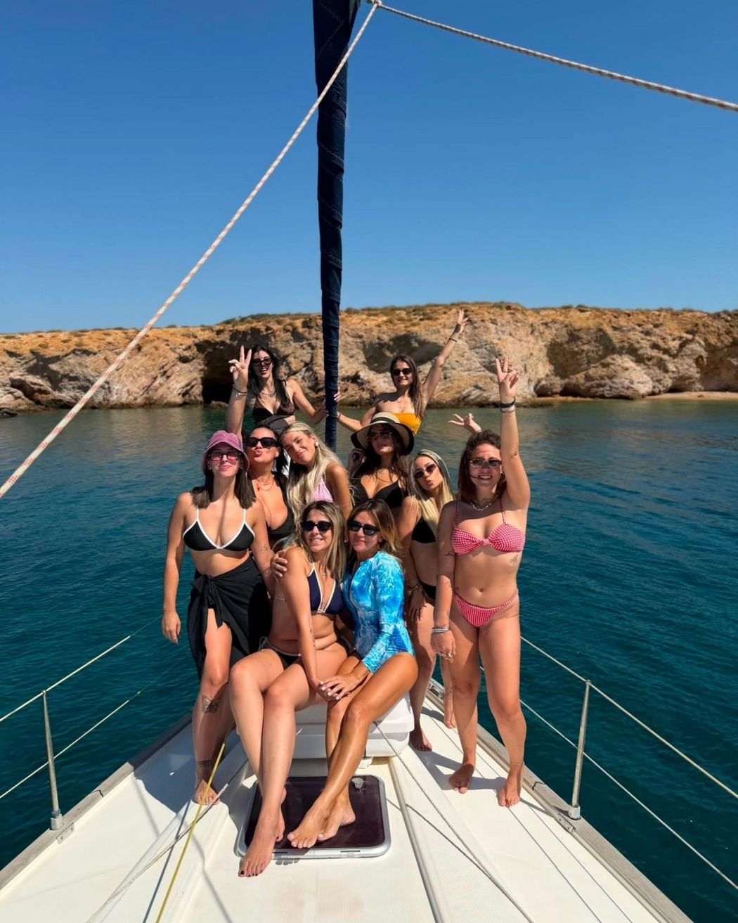 A bachelorette group together on the foredeck at anchor, the shore close behind