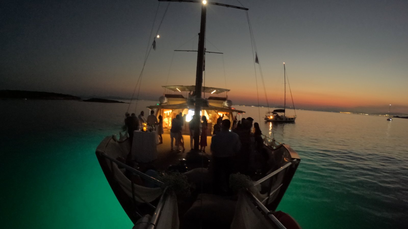The boat lit up at anchor after sunset, the water under it turned green by the lights