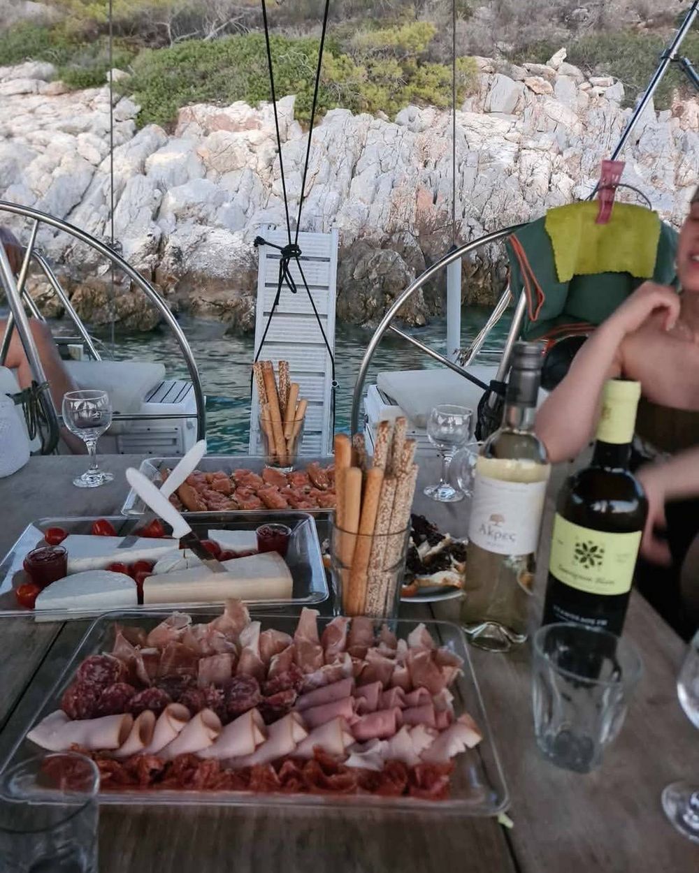 Cheese, cold cuts and wine laid out on the cockpit table, the rocks of the cove close behind