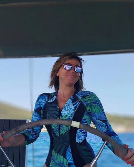 Maria at the wheel under the bimini, open water behind her